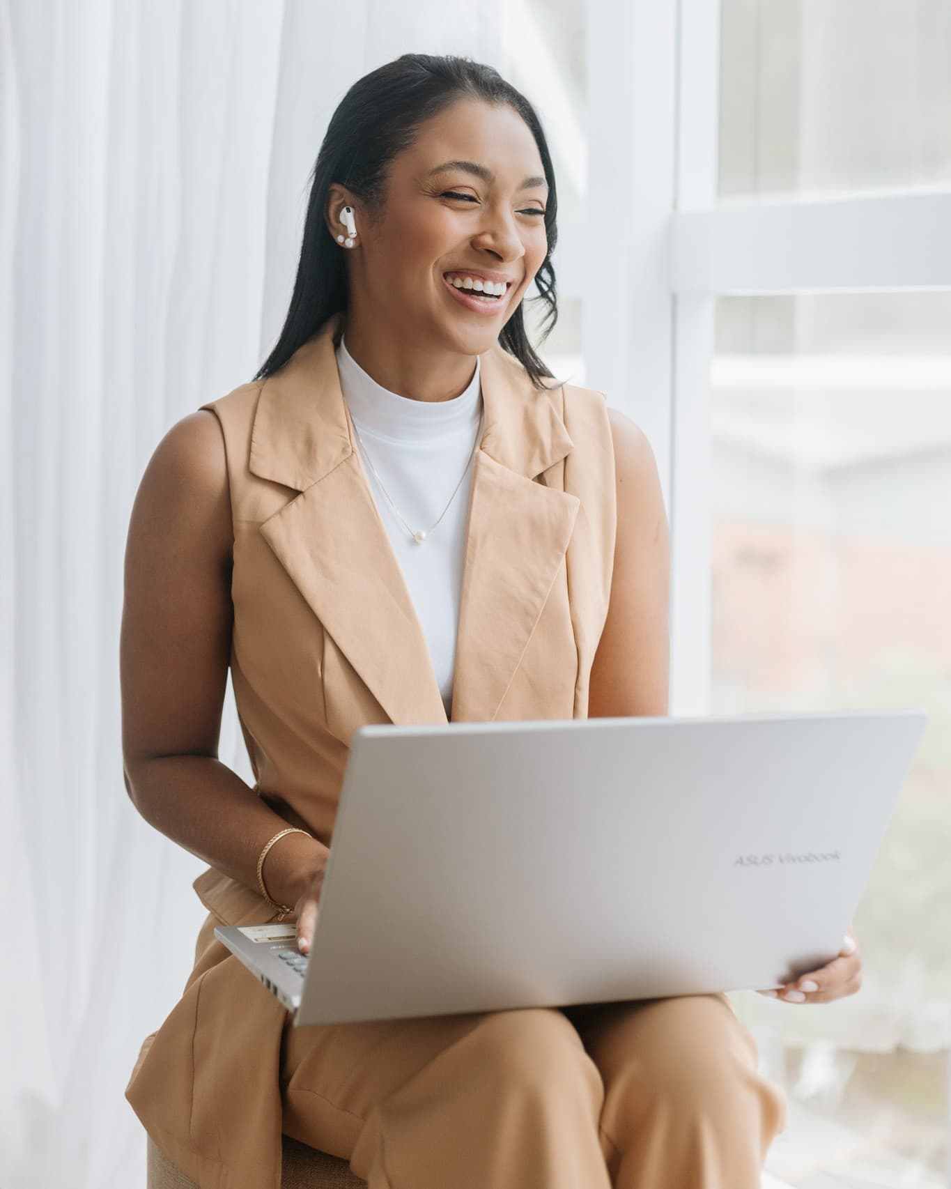 Bruna em atendimento online, com fone e notebook, ao lado de uma janela